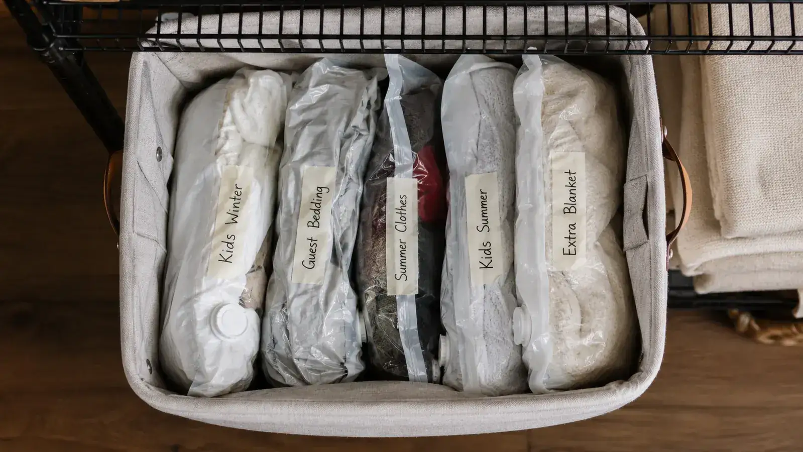 Open storage bin on a closet shelf containing labeled vacuum bags for different household members