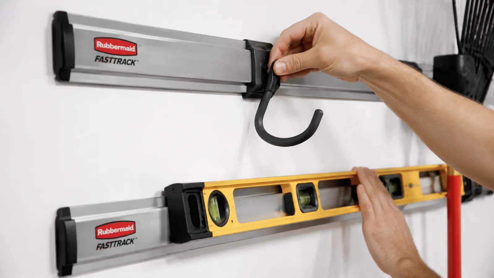 Two Rubbermaid FastTrack rails mounted horizontally on a garage wall with hooks being snapped into place