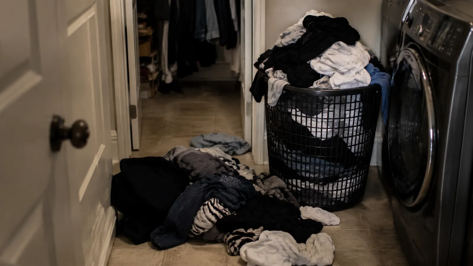 Pile of unsorted laundry on a bathroom floor next to a hamper
