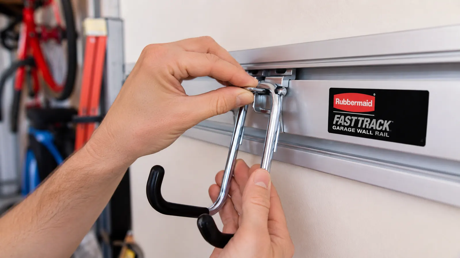 Close-up of a hand sliding a Rubbermaid FastTrack hook onto the horizontal rail, showing the click-lock mechanism
