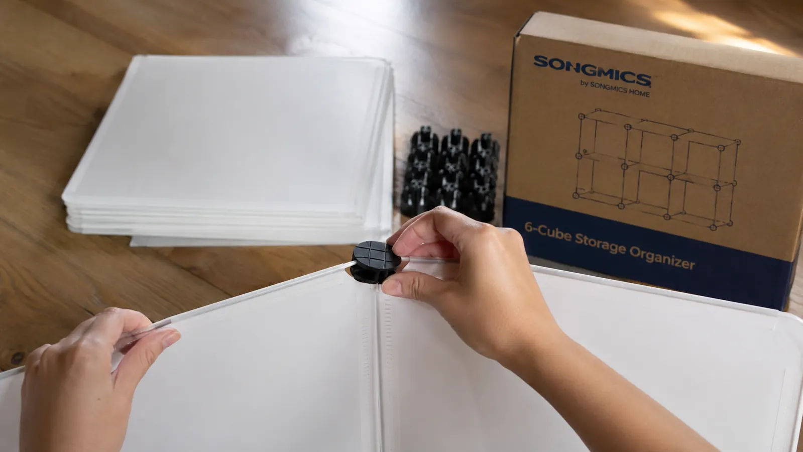 Close-up of plastic connector clips snapping two white cube shelf panels together during assembly on a wood floor
